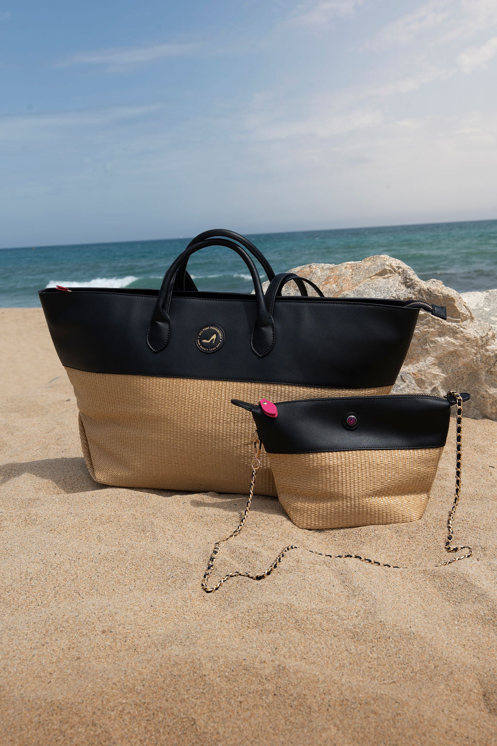 Two bags, one black and one beige with black top, on a sandy beach.