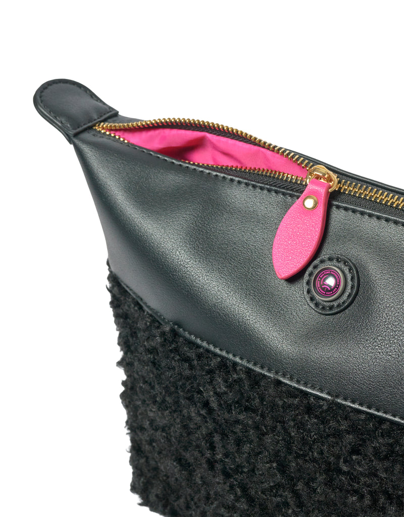 Black faux shearling clutch with gold zipper and pink accents, IMAN brand, close-up view.