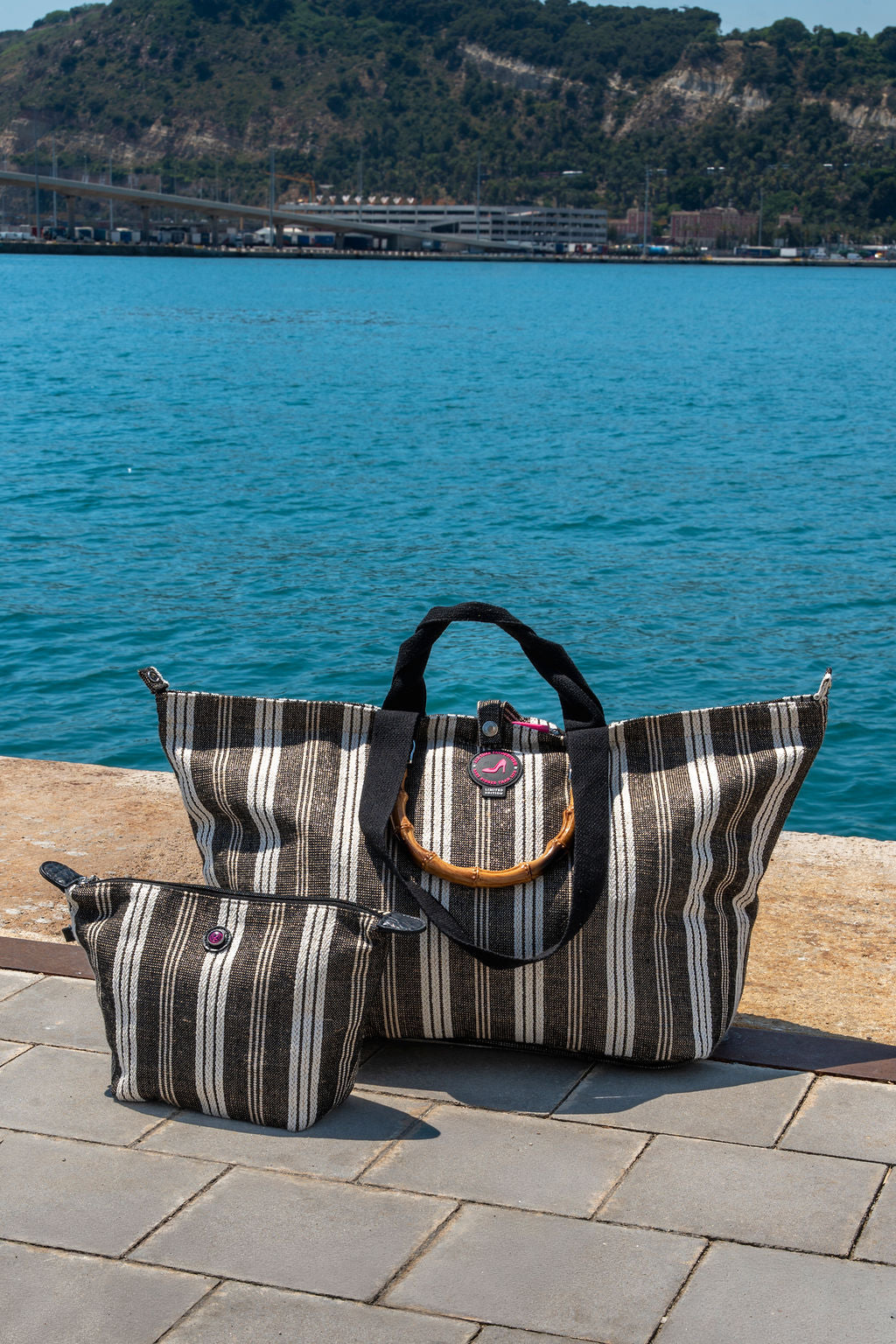 Striped handbags on a stone ledge with a scenic background of water and mountains.