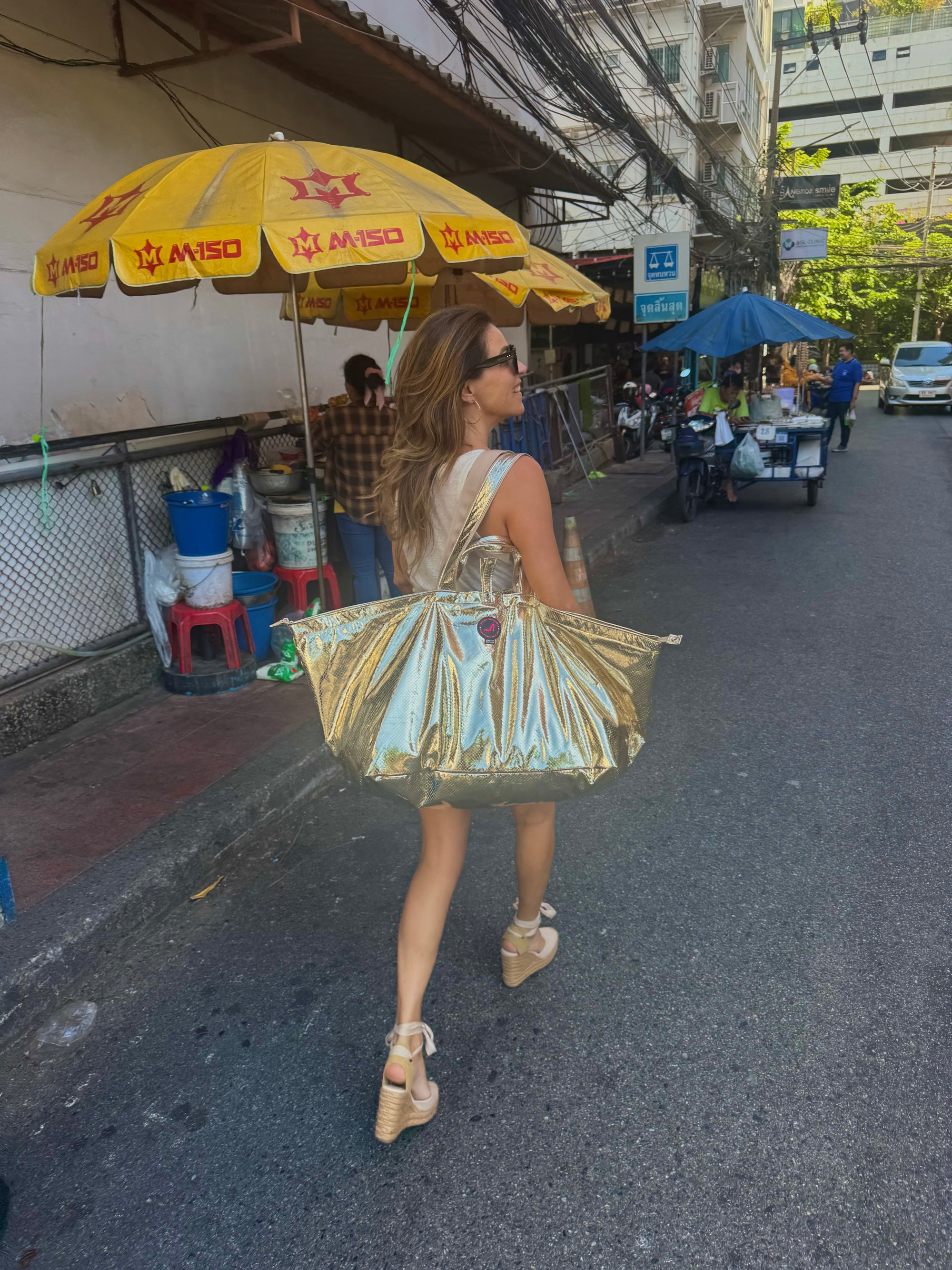 Woman walking through a street in Thailand carrying a large gold python print tote bag over her shoulder