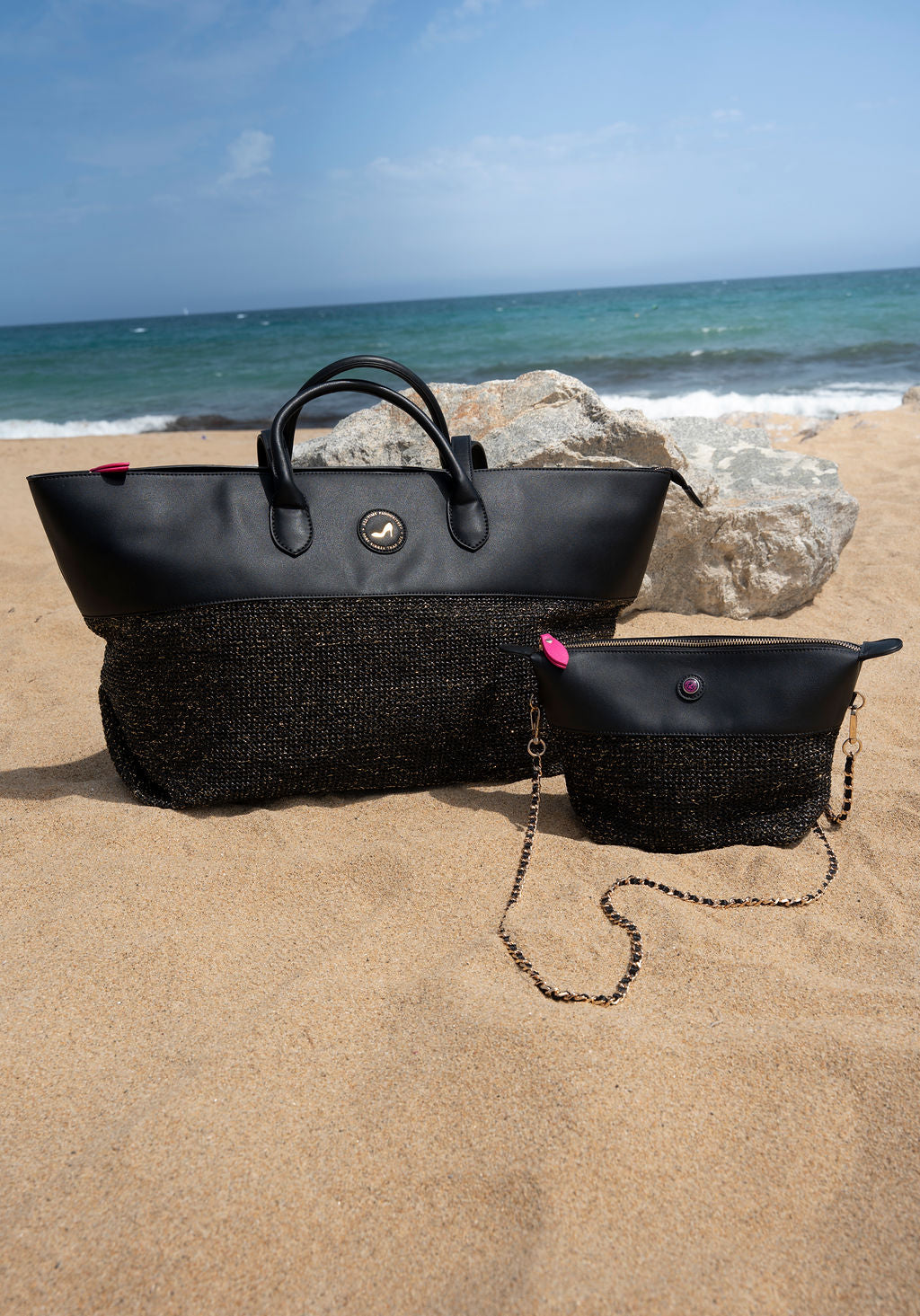 Black handbags of different sizes on a sandy beach with ocean in the background
