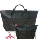 A black leather and woven black-and-gold tote bag shown with a matching small pouch and pink keychain on a white background.