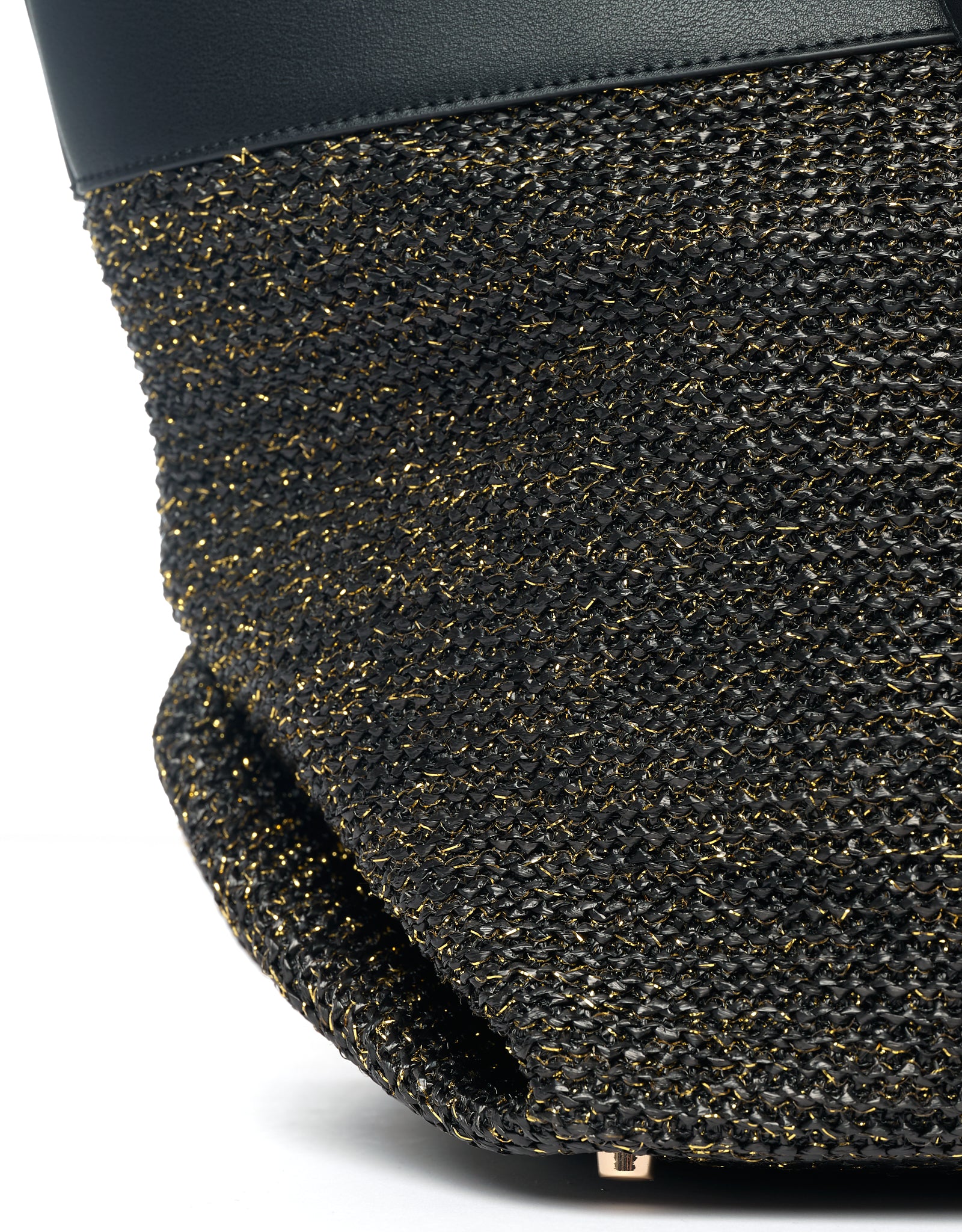 Bottom of black tote bag with protective metal studs and black raffia with gold thread.
