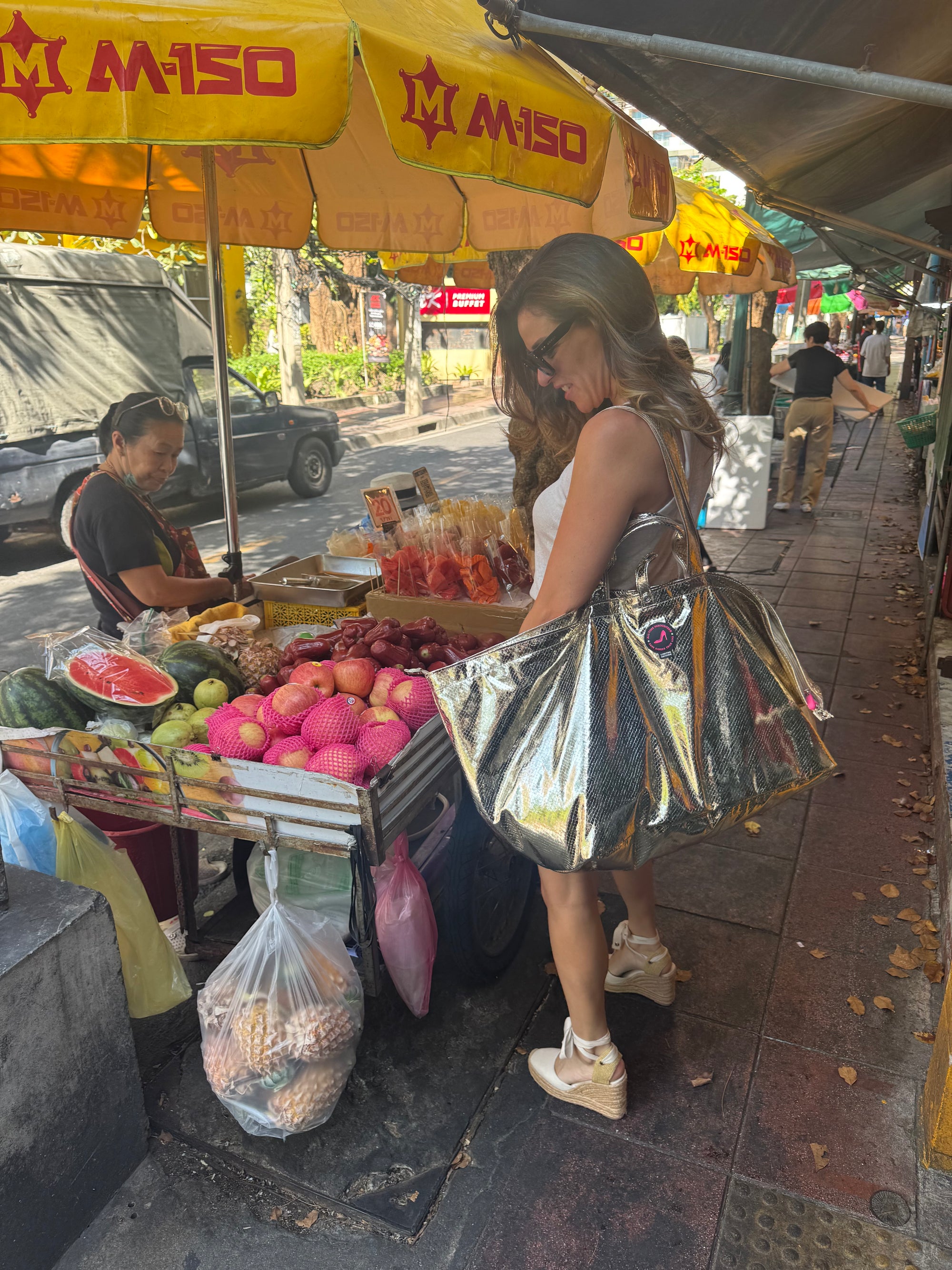 Woman shopping at a street market carrying a large gold metallic tote bag