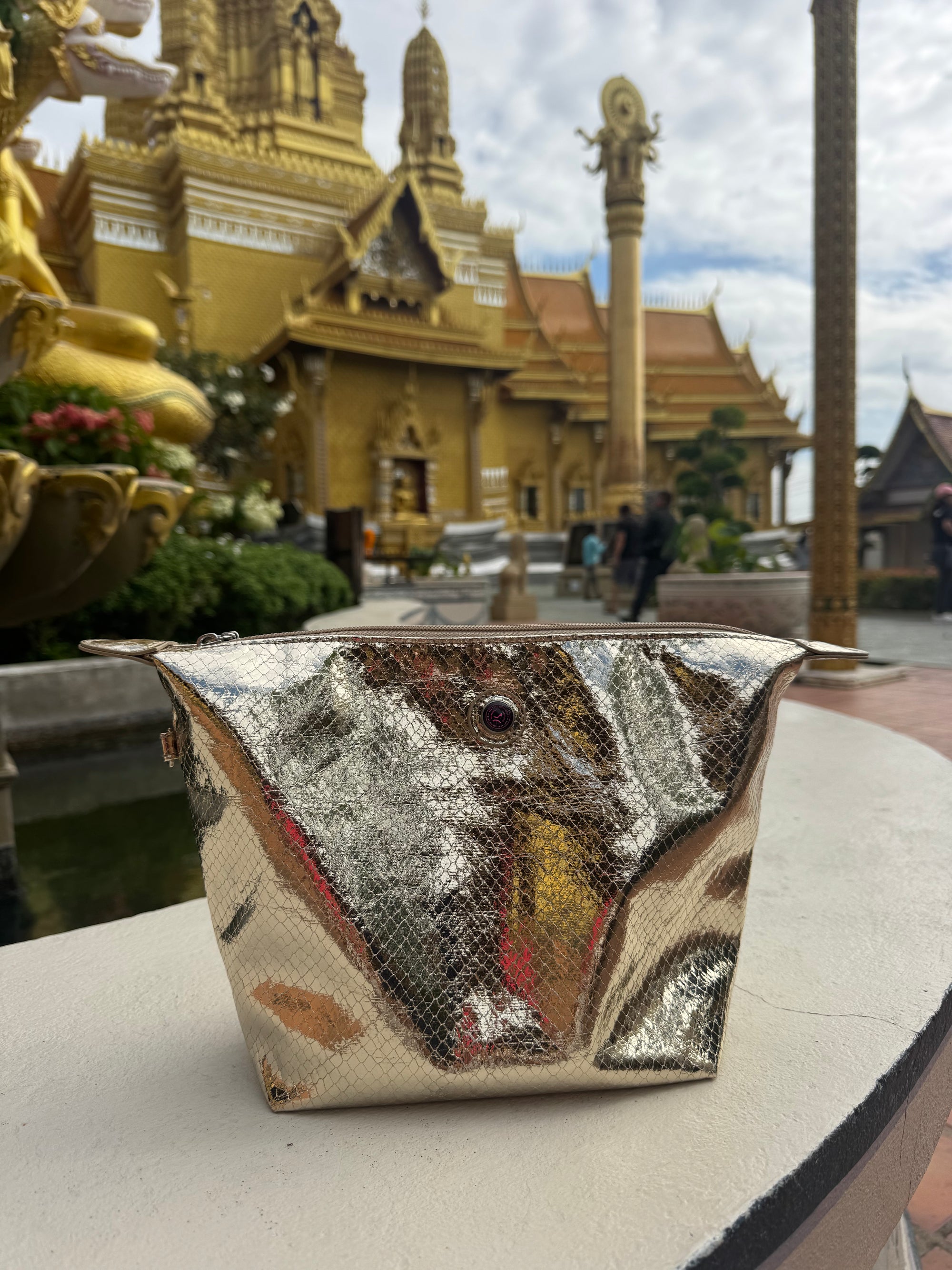 Champagne gold metallic python print toiletry bag photographed in front of a Thai temple