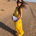 Woman in a yellow dress standing on a desert road holding a white pearl coloured sequin clutch