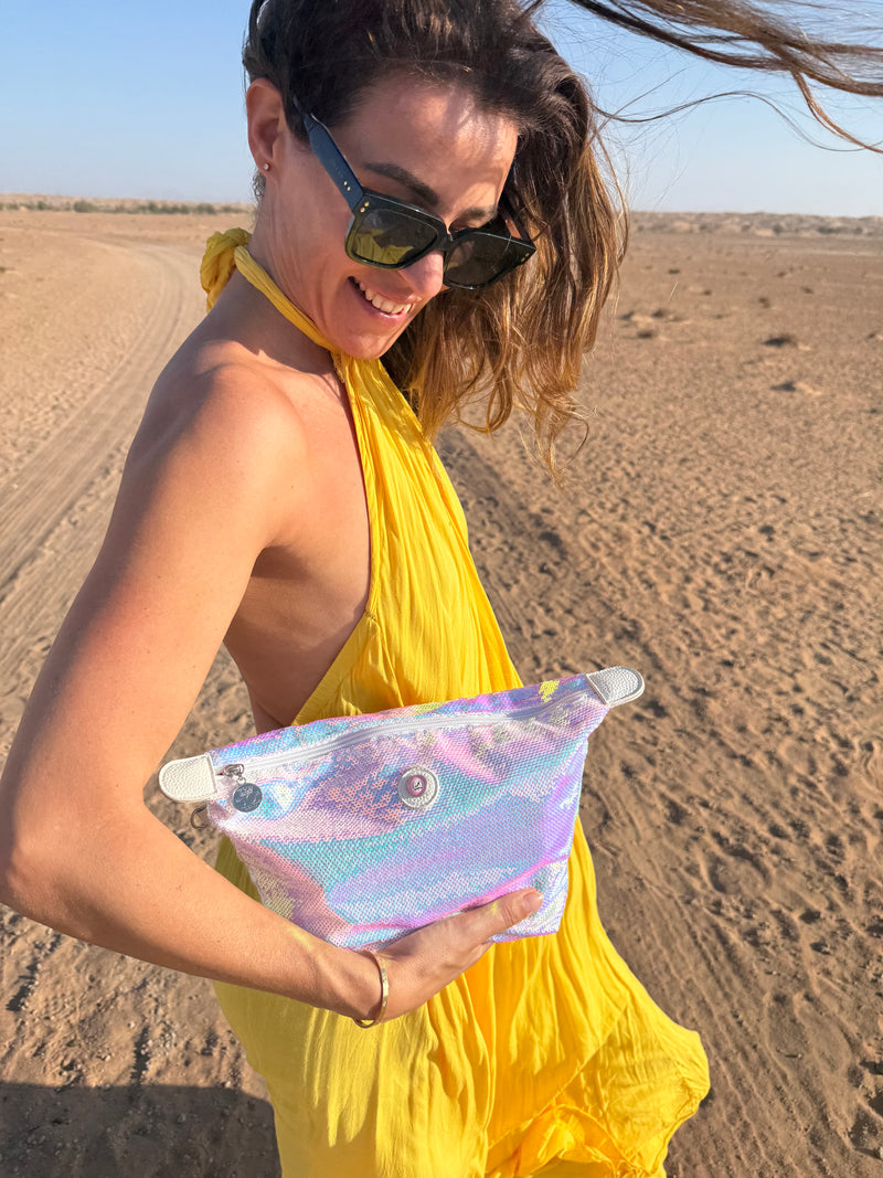 Woman in a yellow dress standing in the dessert showing a white blue pearl coloured toiletry bag