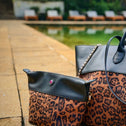 Leopard print handbag with matching bag-in-bag on a stone surface with a blurred garden and pool in the background