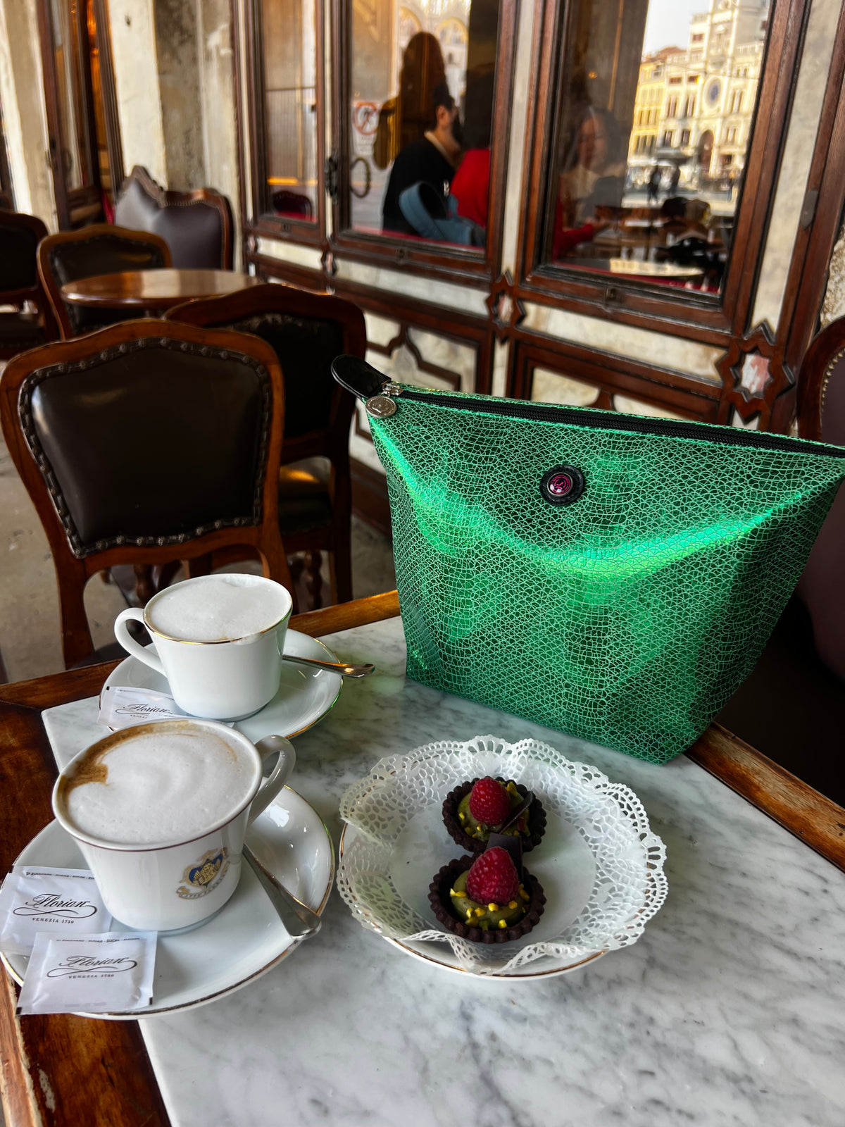 Metallicgroene VENEZIA-toilettas met cappuccino’s en desserts op een tafel in een vintage café-sfeer.