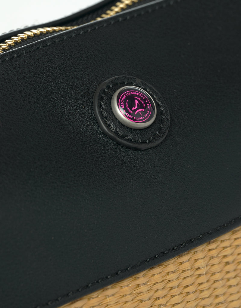 Detail of black vegan leather bag with logo button and beige straw body
