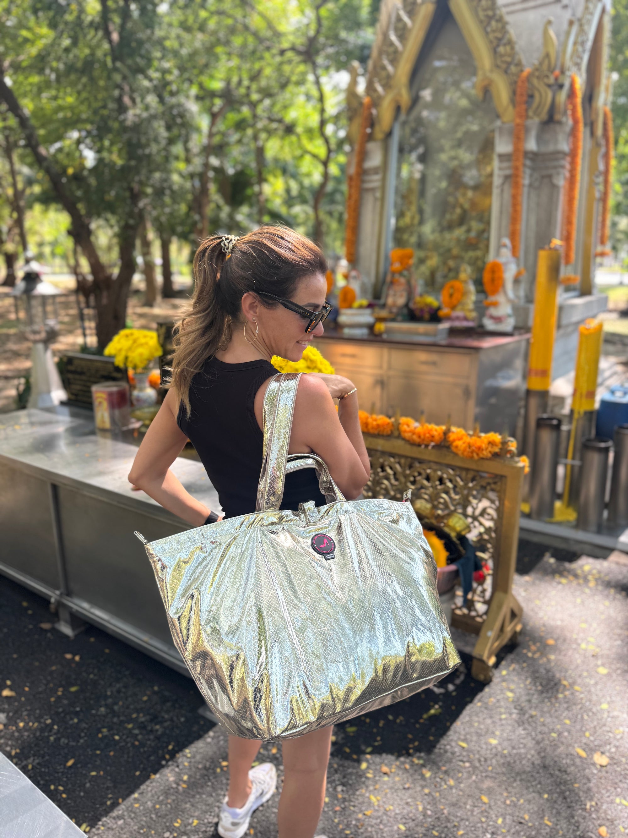 Woman carrying a medium gold metallic tote bag at a small temple in Thailand