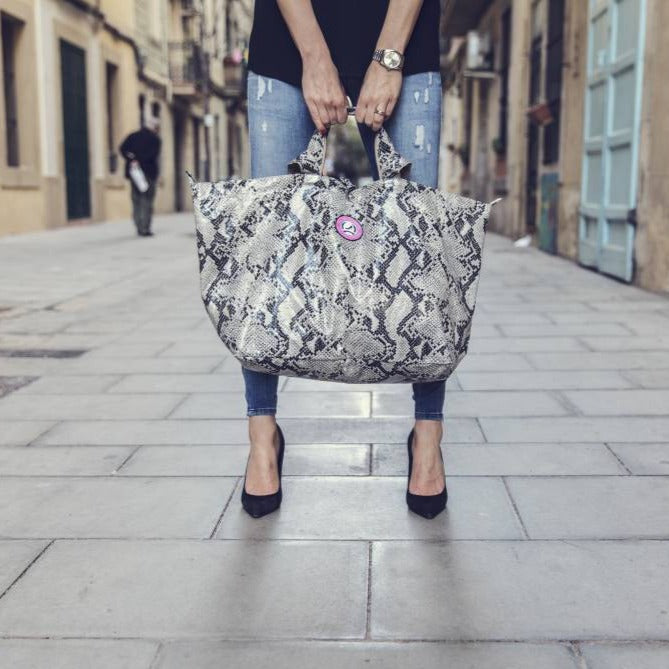 Vrouw in een gescheurde spijkerbroek met een middelgrote leren tas met pythonprint in een straat in de stad, op hakken.