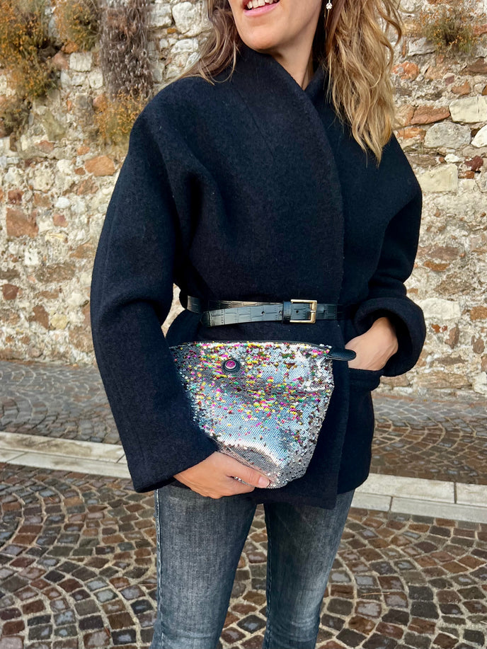 Person wearing a black outfit with a glittery bag against a stone wall background