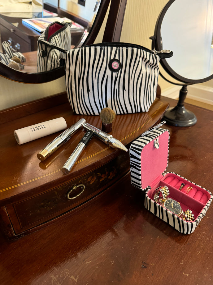 Schmuckkästchen mit Zebra-Muster, dazu eine gestreifte Kosmetiktasche und Kosmetikartikel, die auf einem Schminktisch aus Holz ausgestellt sind.